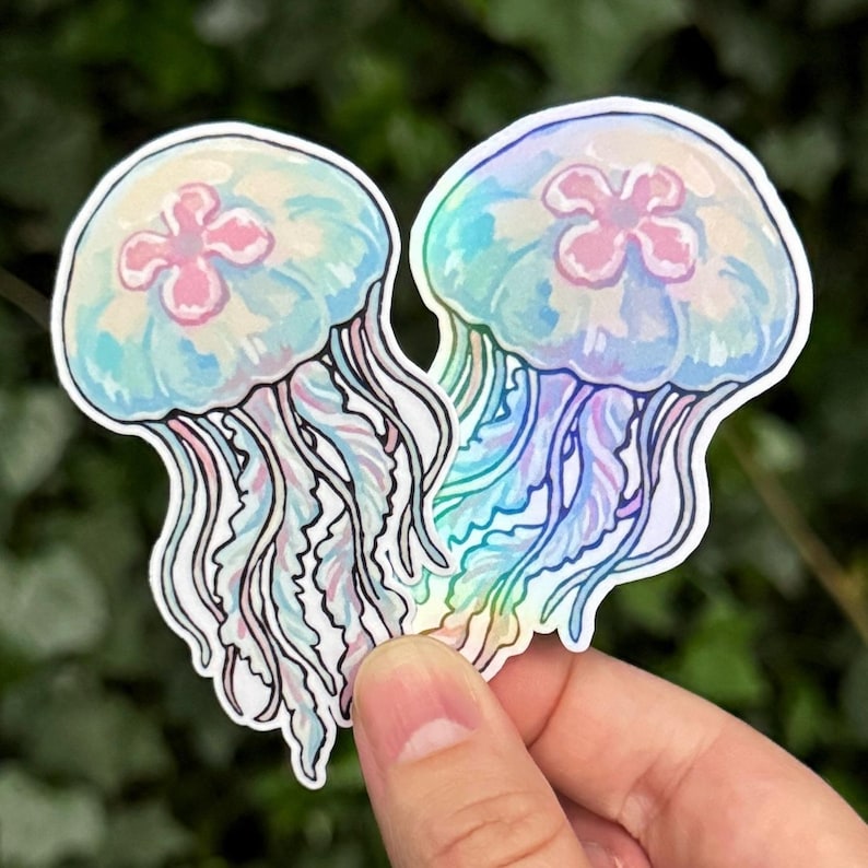 Pu&ograve; includere: Due adesivi fustellati raffiguranti meduse con campane traslucide azzurre e bianco iridescente, centri rosa a quattro lobi e lunghi tentacoli ondulati e fluenti in tonalit&agrave; azzurro pallido, rosa e bianco con un bordo bianco distinto.