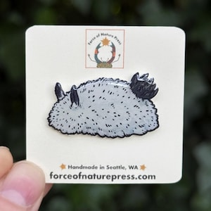 Puede incluir: Un pin de esmalte de nudibranquio gris claro con motas negras y detalles oscuros sobre una tarjeta blanca. La tarjeta incluye el texto Force of Nature Press, un logotipo con un cangrejo, y el texto Handmade in Seattle, WA y forceofnaturepress.com.