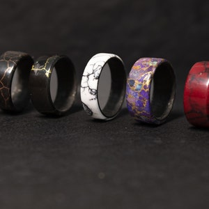 May include: A row of eight colorful rings with different patterns, including black and white, red, purple, and gold. The rings are made of wood and have a smooth, polished finish.