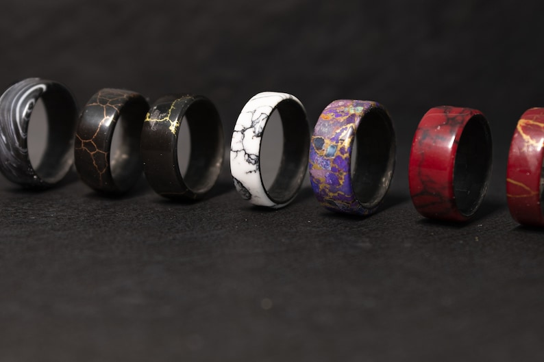 May include: A row of eight colorful rings with different patterns, including black and white, red, purple, and gold. The rings are made of wood and have a smooth, polished finish.