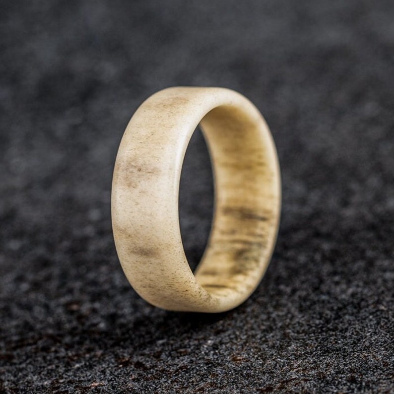 May include: A light-colored ring with a smooth, rounded design. The ring has a natural, organic appearance with subtle variations in color and texture. The ring is made of a light beige material with darker brown streaks.