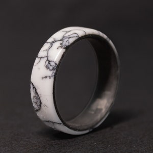 May include: A white and black ring with a marbled design. The ring is made of resin and has a smooth, polished finish.