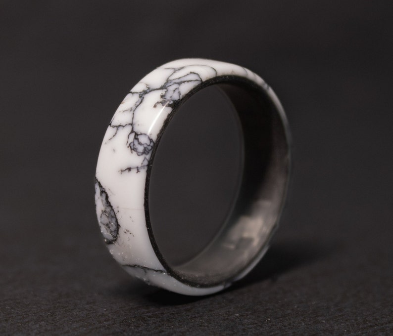 May include: A white and black ring with a marbled design. The ring is made of resin and has a smooth, polished finish.