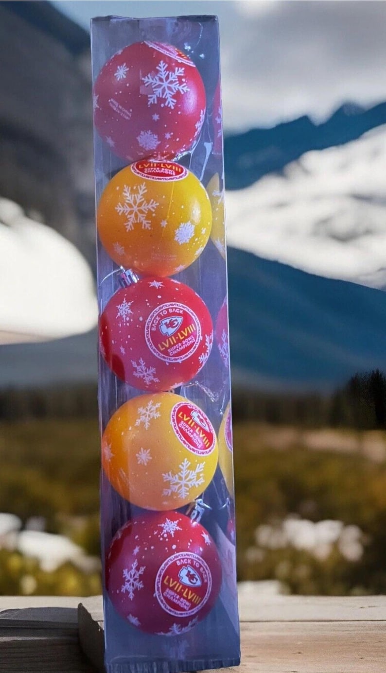 May include: A clear plastic package containing five round Christmas ornaments. The ornaments alternate between red and yellow, each decorated with white snowflakes. The red ornaments have the text "LVII-LVII Super Bowl Champions".