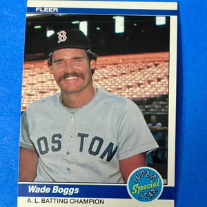 May include: A baseball card featuring Wade Boggs in a Boston Red Sox uniform. The card has a blue border and includes the text "FLEER", "OS TON", "Wade Boggs", and "A. L. BATTING CHAMPION". A "SUPER Special STAR" sticker is also visible.