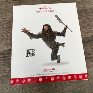 May include: A Hallmark Keepsake Christmas tree ornament featuring Aquaman from Justice League. The figure is in a dynamic pose, holding a trident. The packaging is white with red accents and the Justice League logo.