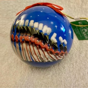 May include: A blue Christmas ornament with a red bow and gold string. The ornament features a marching band illustration with white, red, and black uniforms. The ornament has a Kurt S. Adler tag.