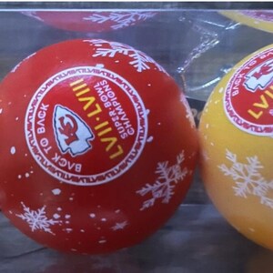 May include: Red and yellow Christmas ornaments with white snowflake designs. Each ornament has a circular sticker with the text "LVII-LVIII Super Bowl Champions Back to Back".