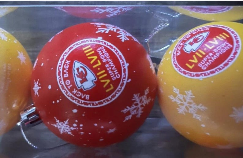 May include: Red and yellow Christmas ornaments with white snowflake designs. Each ornament has a circular sticker with the text "LVII-LVIII Super Bowl Champions Back to Back".