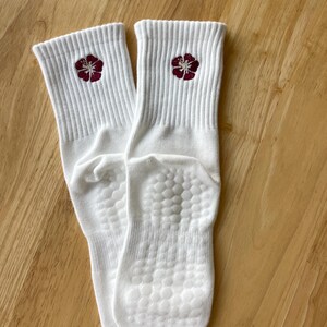 K&ouml;nnte beinhalten: Ein Paar wei&szlig;e Socken mit geripptem B&uuml;ndchen und einer bordeauxfarbenen Blume auf jeder Socke. Die Sohlen haben ein strukturiertes, rutschfestes Muster. Die Socken sind aus weichem, bequemem Material.