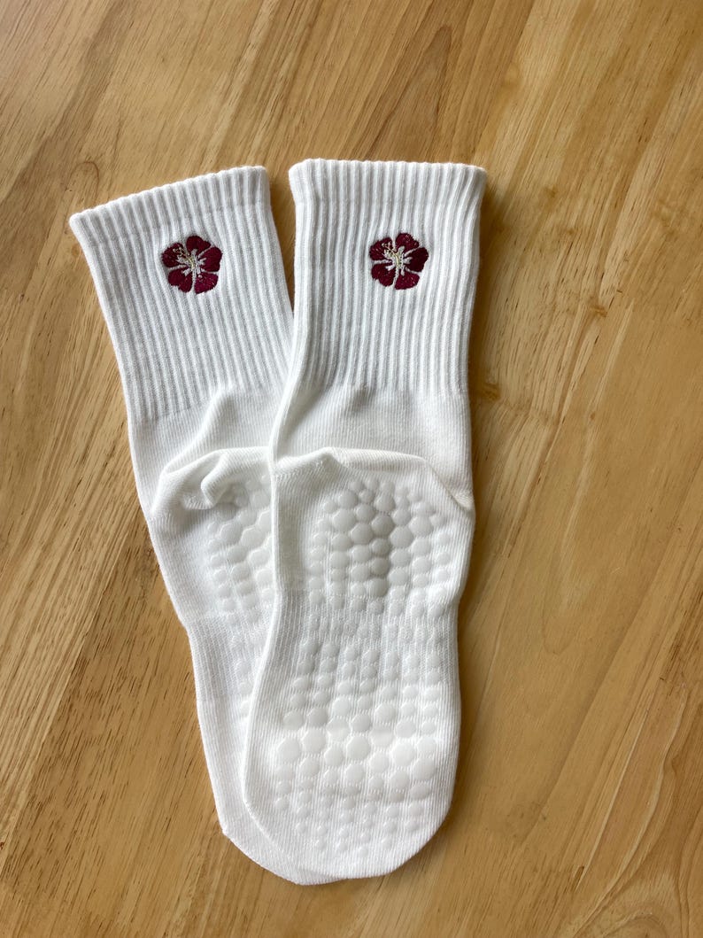 K&ouml;nnte beinhalten: Ein Paar wei&szlig;e Socken mit geripptem B&uuml;ndchen und einer bordeauxfarbenen Blume auf jeder Socke. Die Sohlen haben ein strukturiertes, rutschfestes Muster. Die Socken sind aus weichem, bequemem Material.