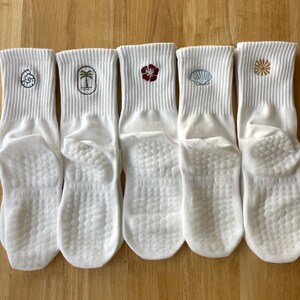 K&ouml;nnte beinhalten: F&uuml;nf wei&szlig;e Kn&ouml;chelsocken mit gestickten Designs. Jede Socke hat ein anderes Design: eine Muschel, eine Palme, eine Blume, eine Muschel und ein Sternenmuster. Die Socken haben eine strukturierte Sohle.