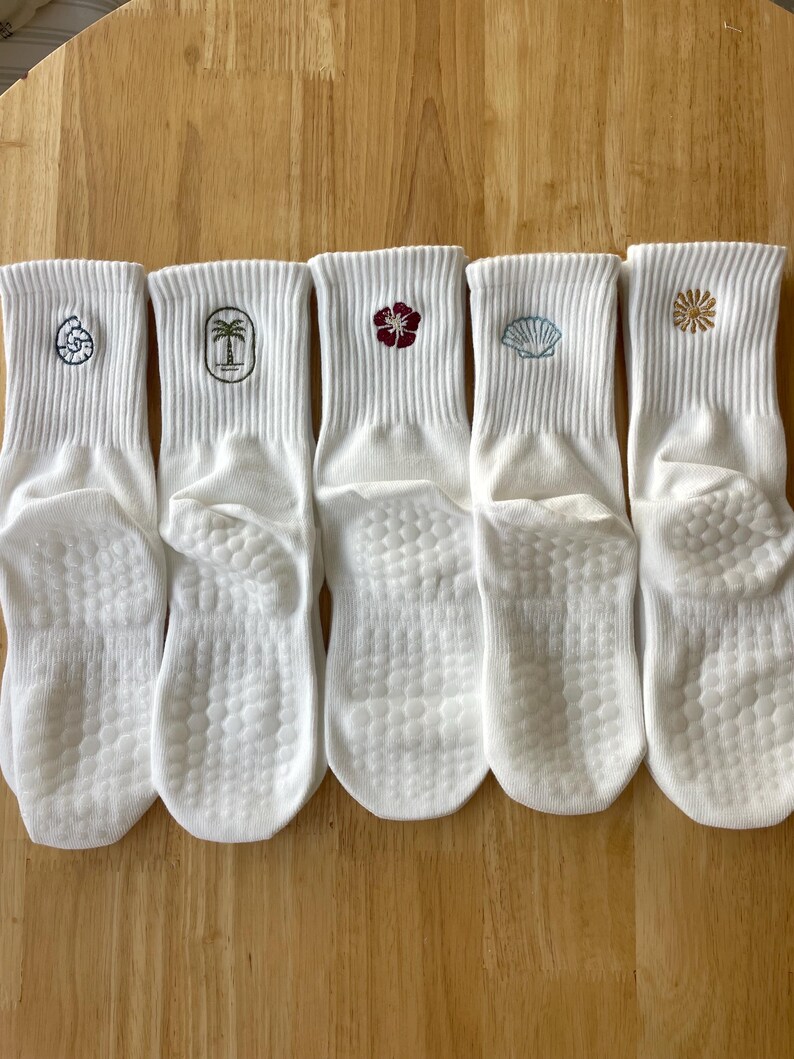 K&ouml;nnte beinhalten: F&uuml;nf wei&szlig;e Kn&ouml;chelsocken mit gestickten Designs. Jede Socke hat ein anderes Design: eine Muschel, eine Palme, eine Blume, eine Muschel und ein Sternenmuster. Die Socken haben eine strukturierte Sohle.
