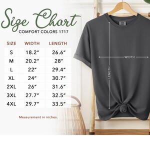 May include: A dark gray Comfort Colors 1717 t-shirt with a size chart. The chart shows measurements in inches for sizes S to 4XL. The shirt's width and length are indicated with arrows. The text "Size Chart" is at the top.