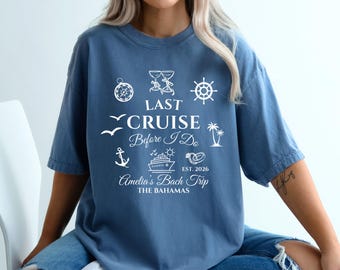 Può includere: Una maglietta blu con testo e grafica bianchi. La maglietta presenta le parole "LAST CRUISE Before I Do" con illustrazioni a tema nautico, tra cui una nave, un'ancora e una palma. Sono inclusi anche i testi "Amelia's Bach Trip" e "THE BAHAMAS".