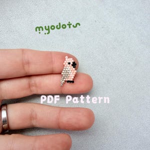 Op de afbeelding: Een kleine, geborduurde uil in roze, zilver en zwart, vastgehouden tussen vingers. De tekst "myodots" in groen staat boven de uil en "PDF Pattern" in roze eronder.