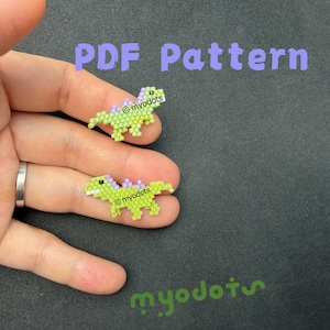 May include: Two beaded dinosaur figures in shades of green and purple are displayed on a hand. The dinosaurs have a pixelated design. The text "PDF Pattern" is above the dinosaurs, and the myodots logo is below.