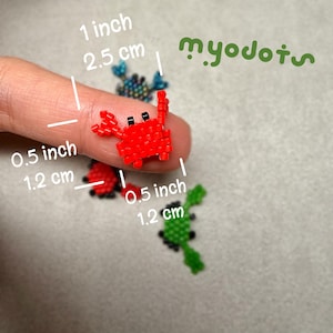 May include: Tiny beaded crab figurines in red, black, and green. The red crab is 0.5 inches (1.2 cm) wide. The image also shows a blue crab and the text "myodots".