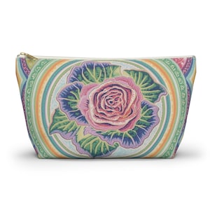 Puede incluir: Un neceser con cremallera con un diseño detallado de rosa. La rosa es rosa, rodeada de hojas verdes y un fondo azul y morado. La bolsa tiene una cremallera dorada y un borde colorido con dibujos.