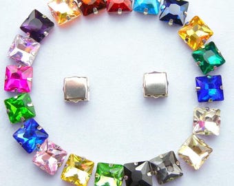 May include: A selection of square-cut, multi-coloured rhinestones arranged in a circular pattern, resembling a smiley face. The gems are in various colours, including purple, orange, red, blue, and green. Two silver-coloured square studs are in the centre.