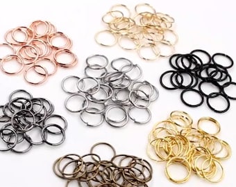 May include: A collection of small metal jump rings in various colors, including rose gold, gold, silver, black, and bronze. The rings are arranged in separate piles, showcasing their different finishes and tones. These rings are likely used for jewelry making or crafting.