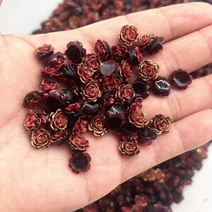 Può includere: Una collezione di piccole perline a forma di rosa color bordeaux con bordi dorati. Le perline sono raggruppate, mostrando il loro intricato design floreale. Queste perline decorative sono ideali per l'artigianato e la creazione di gioielli.