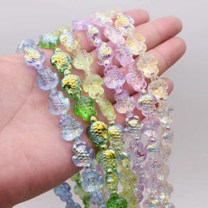 May include: Several strands of iridescent turtle-shaped beads in shades of blue, green, yellow, and purple. The beads are strung together, creating a shimmering effect. These beads are suitable for jewellery making and craft projects.