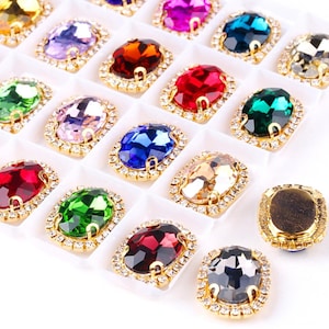 Puede incluir: Una colección de pedrería ovalada y colorida en una bandeja blanca. Cada pedrería es de un color diferente, incluyendo amarillo, morado, rojo y verde, y está rodeada por un marco de metal dorado con pequeños cristales transparentes.