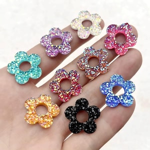 以下が含まれることがあります： キラキラ光る、様々な色の花型の装飾品のコレクション。花の中心には穴があり、ピンク、青、紫、オレンジなど様々な色があります。キラキラ光る効果があり、視覚的に魅力的です。