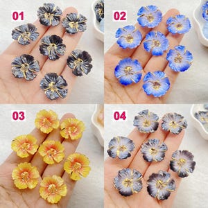 May include: A collection of flower-shaped beads in four different color schemes. The beads have a translucent appearance with gold-colored accents. The color schemes include dark blue, light blue, yellow, and a mix of gray and purple.