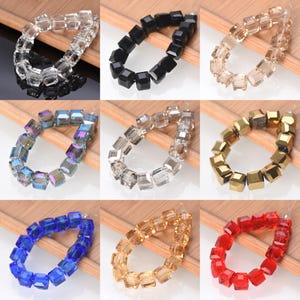 May include: A collection of square-cut beads in various colors, including clear, black, gold, blue, and red. The beads are strung together, showcasing their faceted surfaces and potential for jewelry making or crafting projects.