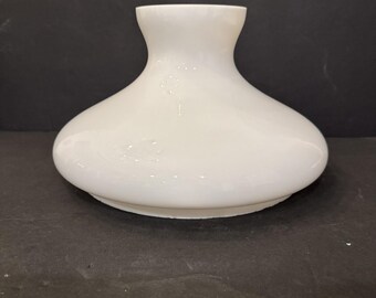 Puede incluir: Una pantalla de lámpara de vidrio opalino blanco con un cuerpo redondeado y abombado, y un cuello abierto y ensanchado. El vidrio tiene una apariencia semitranslúcida con un acabado brillante, con una base ancha que se estrecha hacia arriba.