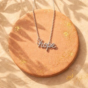 A delicate silver-tone pendant featuring the word HOPE in cursive