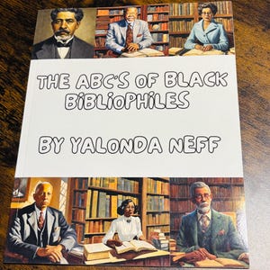 May include: A book titled "THE ABC'S OF BLACK BIBLIOPHILES" by Yalonda Neff. The cover features portraits of people and bookshelves. The book is on a dark wooden surface.