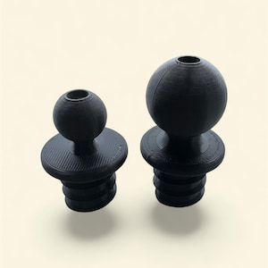 May include: Two black bottle stoppers. One is smaller with a round top and the other is larger with a spherical top. Both have a ridged base and a threaded design for insertion into a bottle. The stoppers are made of a matte black material.
