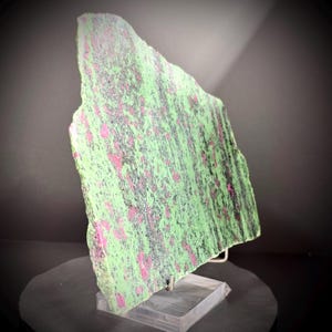 May include: A flat, irregularly shaped slab of zoisite mineral featuring a vibrant lime green base color. The surface is speckled with distinct, scattered patches of deep magenta ruby and streaks of dark, charcoal-colored hornblende inclusions.