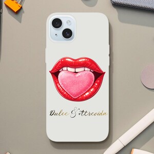 May include: A white phone case featuring a graphic of red lips with a pink heart-shaped tongue. The text "Dulce & Atrevida" is printed in gold script below the lips. The case is surrounded by office supplies.
