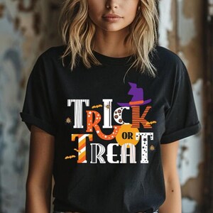 May include: A black short-sleeved t-shirt featuring the text Trick or Treat in a multi-colored, patterned font. The design includes a purple witch hat, small orange bats, and star motifs integrated into the lettering on the front of the shirt.