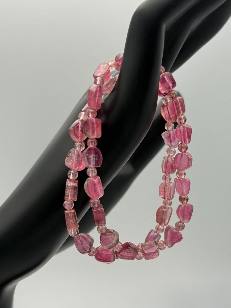 May include: A double-strand bracelet featuring pink tourmaline beads. The beads are a mix of irregular, faceted shapes and smaller, round beads. The bracelet is displayed against a black background, highlighting the pink hues of the gemstones. The bracelet is a piece of jewelry.