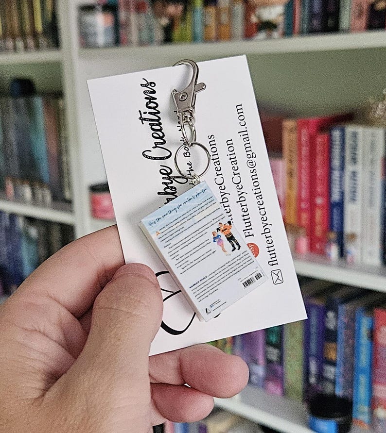 May include: A miniature book keychain with a silver key chain. The book is a paperback with a white cover and a colorful image of a couple on the back. The text on the back of the book reads "Only the one thing you can't control is how you choose to react to it."