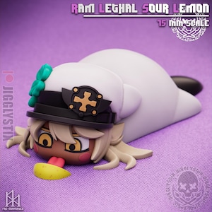 May include: A figurine of a character with tan skin, blonde hair, and a white hat with a black brim and gold cross emblem. The character is lying down, with a yellow lemon slice and the text "RAM LETHAL SOUR LEMON".