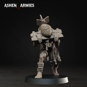 May include: A grey miniature figure from Ashen Armies featuring a character with a stitched sack head, wearing a wooden pillory around the neck and shoulders, with a large bomb-like object strapped to the back and rope bindings on the legs.