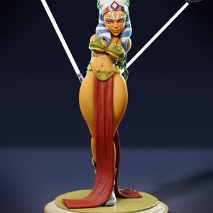 May include: A detailed figurine of a female character with blue and white head tails, wearing a green and gold top, a red skirt, and white boots. The figure is holding two white lightsabers and stands on a wooden base. The figurine is a collectible item.