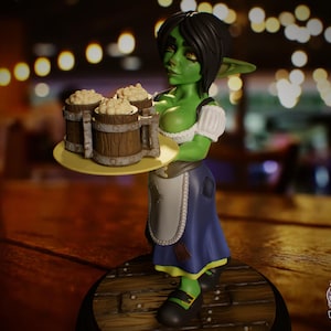 May include: A figurine of a green-skinned goblin waitress holding a tray with three wooden beer mugs filled with foam. She wears a white blouse, blue apron, and black shoes. The figurine stands on a wooden base.