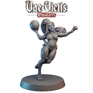 May include: A gray miniature figurine of a woman in a bikini, holding a ball and reaching out. The figurine is on a round base. The text "Vae Victis Miniatures" is above the figurine.