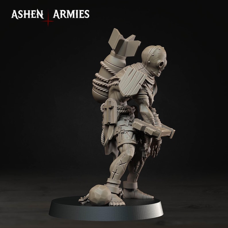 May include: A light brown miniature figurine of a humanoid creature wearing a helmet and carrying a large bomb on its back with rope bindings. The figure holds a rectangular object and stands on a circular base, with the text ASHEN ARMIES visible.