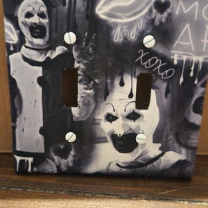 Könnte beinhalten: Schwarz-weiße Lichtschalterabdeckung mit Horror-Motiv. Die Abdeckung hat zwei Schalteröffnungen und weiße Schrauben. Das Design umfasst ein Clown-Gesicht, tropfendes Blut und das Wort "xoxo".