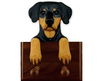 May include: A wooden wall hook featuring a black and tan Doberman Pinscher dog head with its paws hanging over the edge of the hook. The hook has two brown wooden knobs.