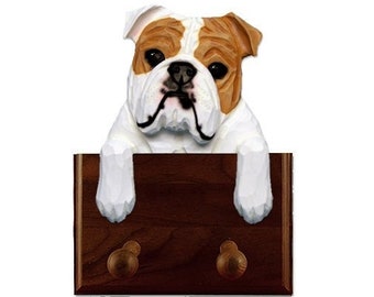 May include: A wooden coat rack featuring a carved bulldog peeking over the top. The rack has two hooks and a dark brown stain.