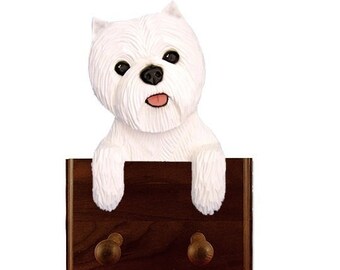 May include: White West Highland Terrier dog figurine peeking over a wooden double hook coat rack. The dog is white with black eyes and a pink tongue. The hook is dark brown with two wooden knobs.